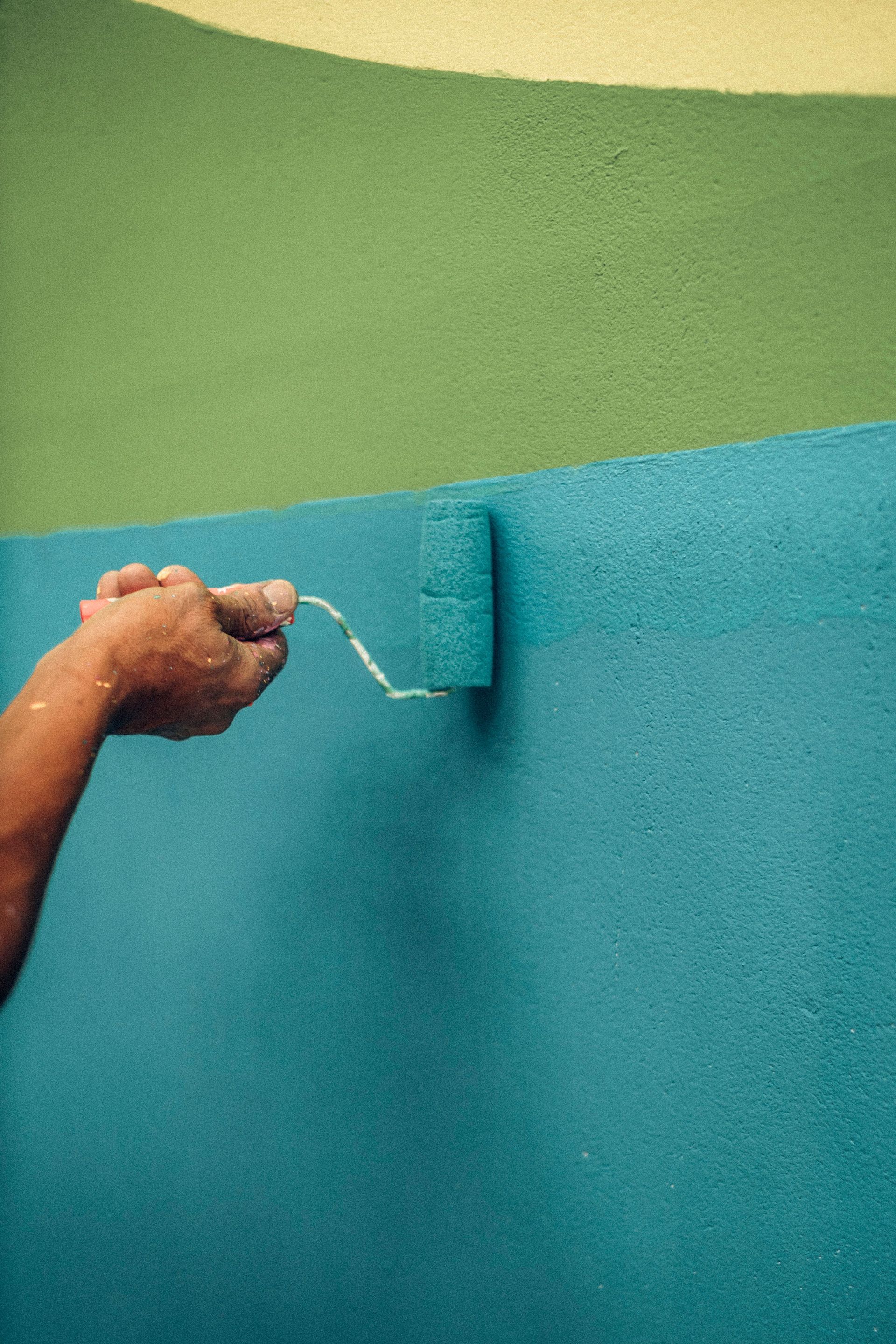 A person using a roller brush to paint a wall with blue and green colors, capturing a renovation moment.