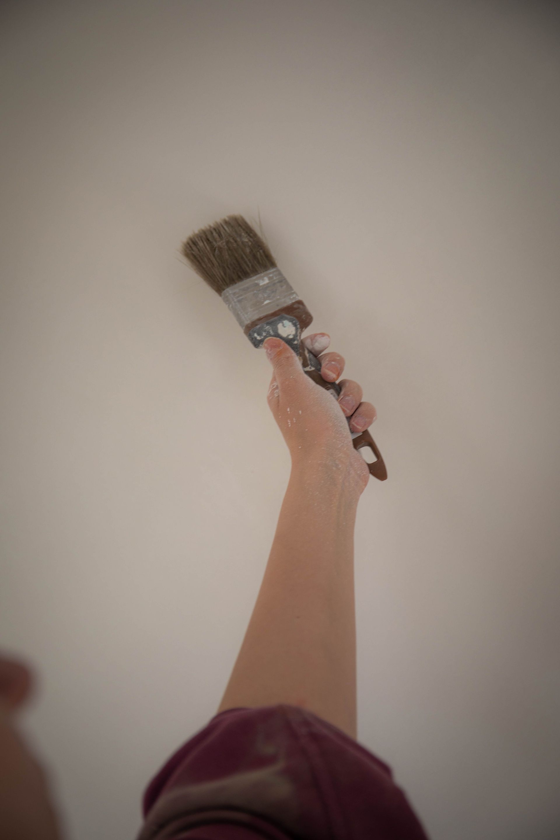 A person's hand holding a paintbrush painting a white wall indoors, showcasing DIY home improvement.